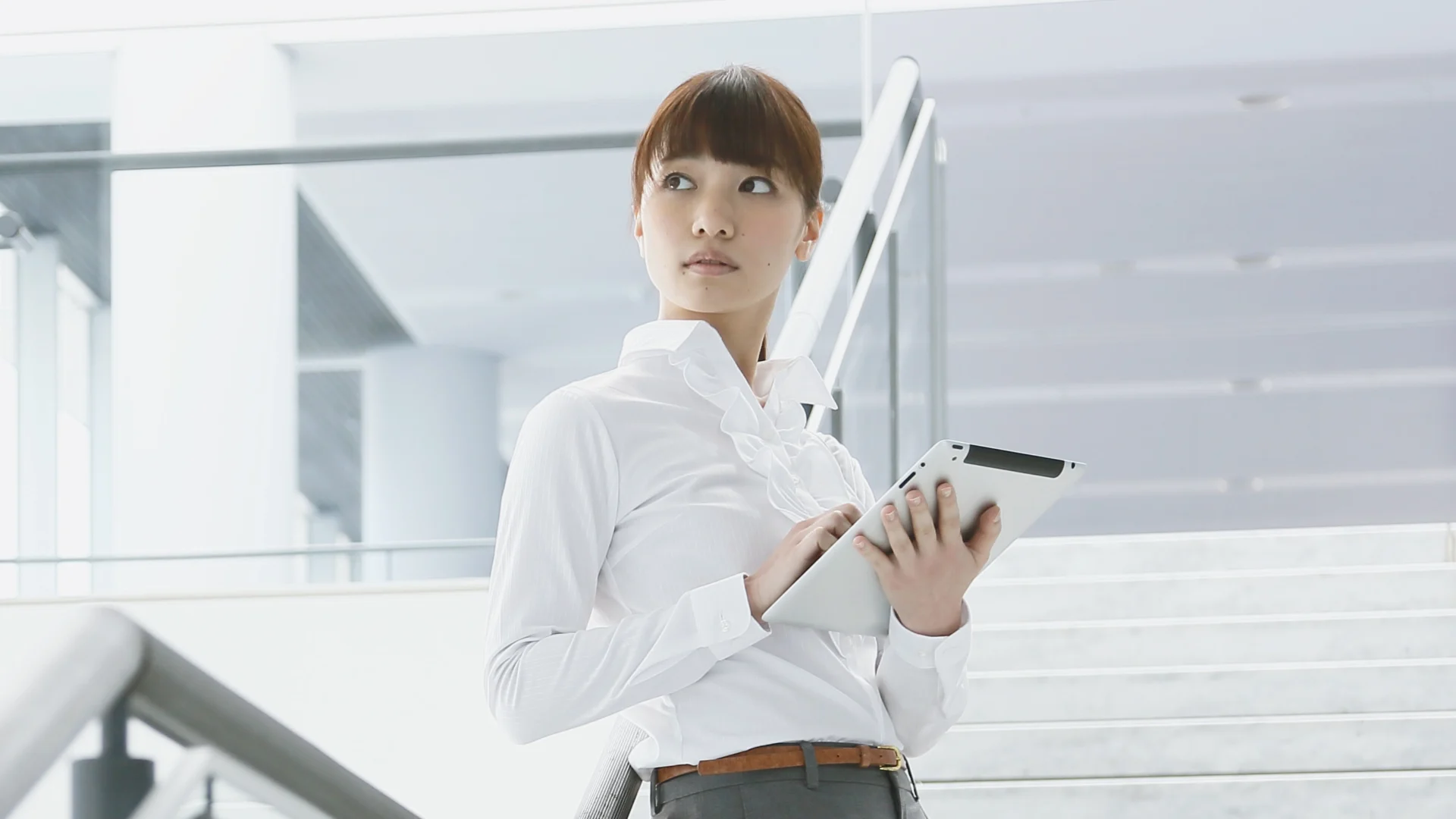 Frau auf Innentreppe eines modernen Bürogebäudes, die mit einem Tablet arbeitet, xpecto Software für Assetmanagement und Sachwerte sichtbar.